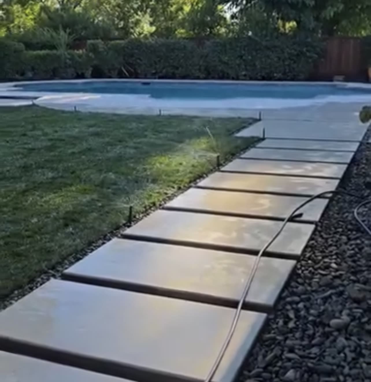 Finished concrete walkway with rock border and new lawn beside a pool