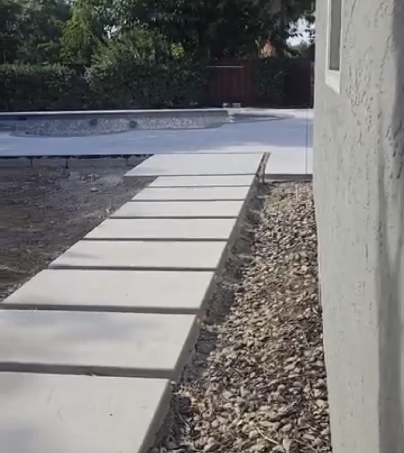Freshly poured concrete walkway pads beside a pool with bare dirt alongside
