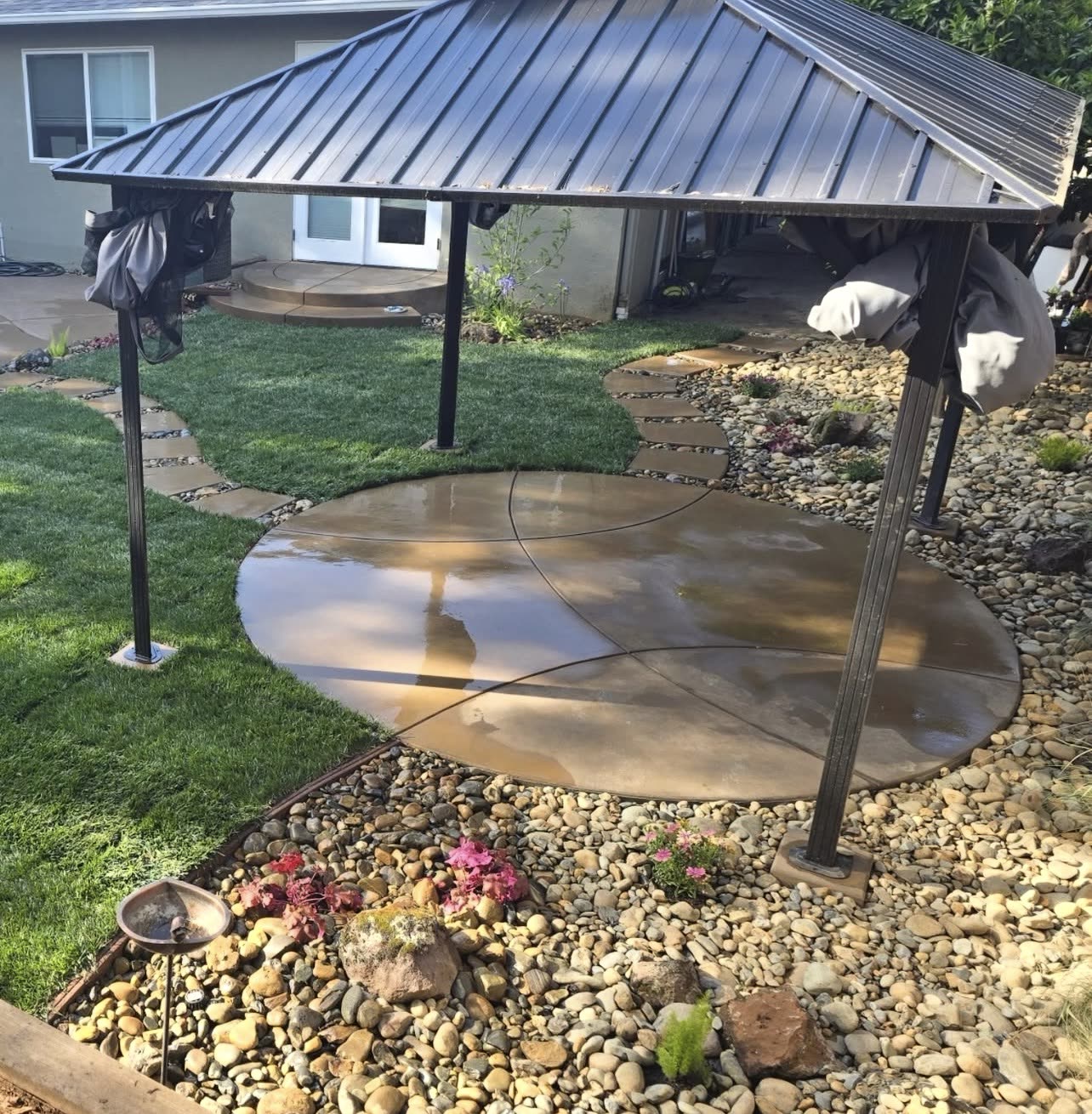 Circular stained concrete patio under a metal gazebo with a stepping stone path